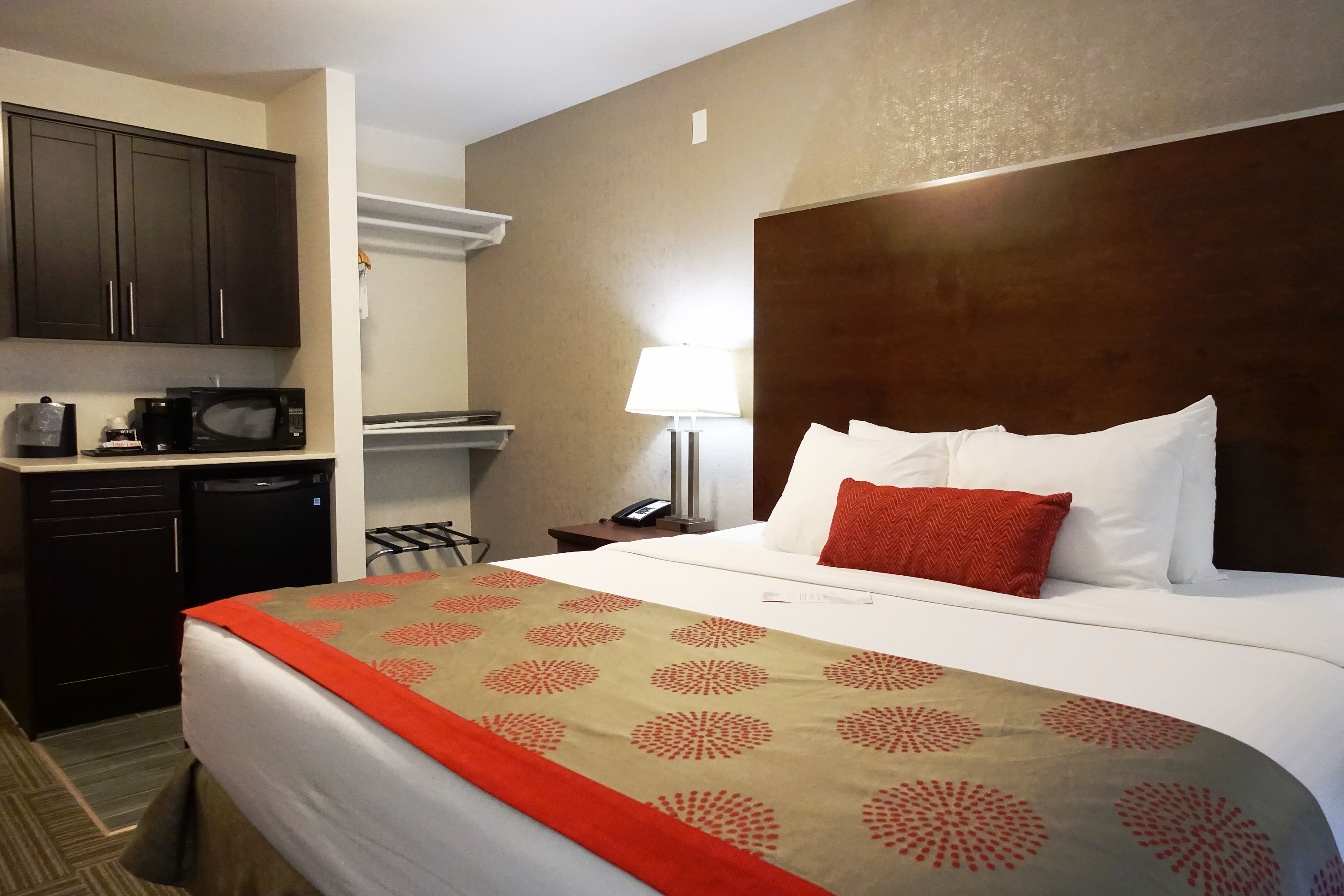 A hotel room with a bed, a desk with a microwave, a lamp, and a telephone.