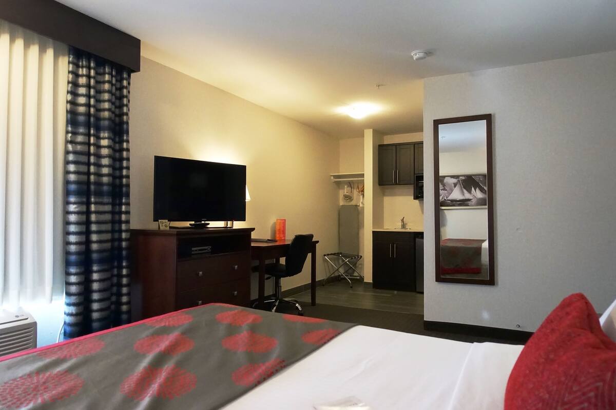Une chambre d’hôtel comprenant un lit, un bureau avec une chaise, une télévision, un miroir et une kitchenette.