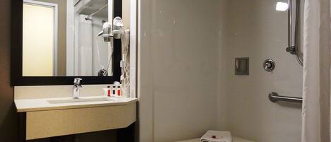A bathroom with a sink, mirror, shower, and a bench with a towel.