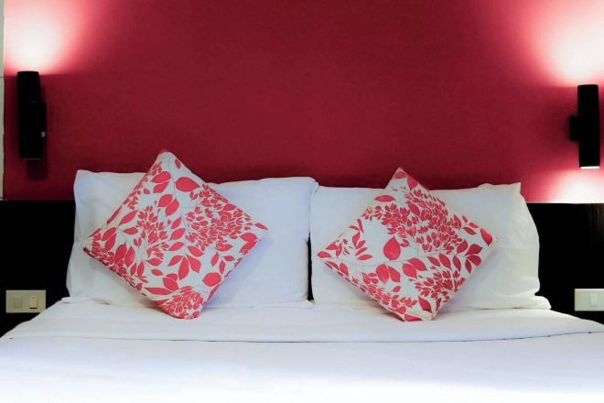 A bed with white bedding and two pillows with a red floral pattern.