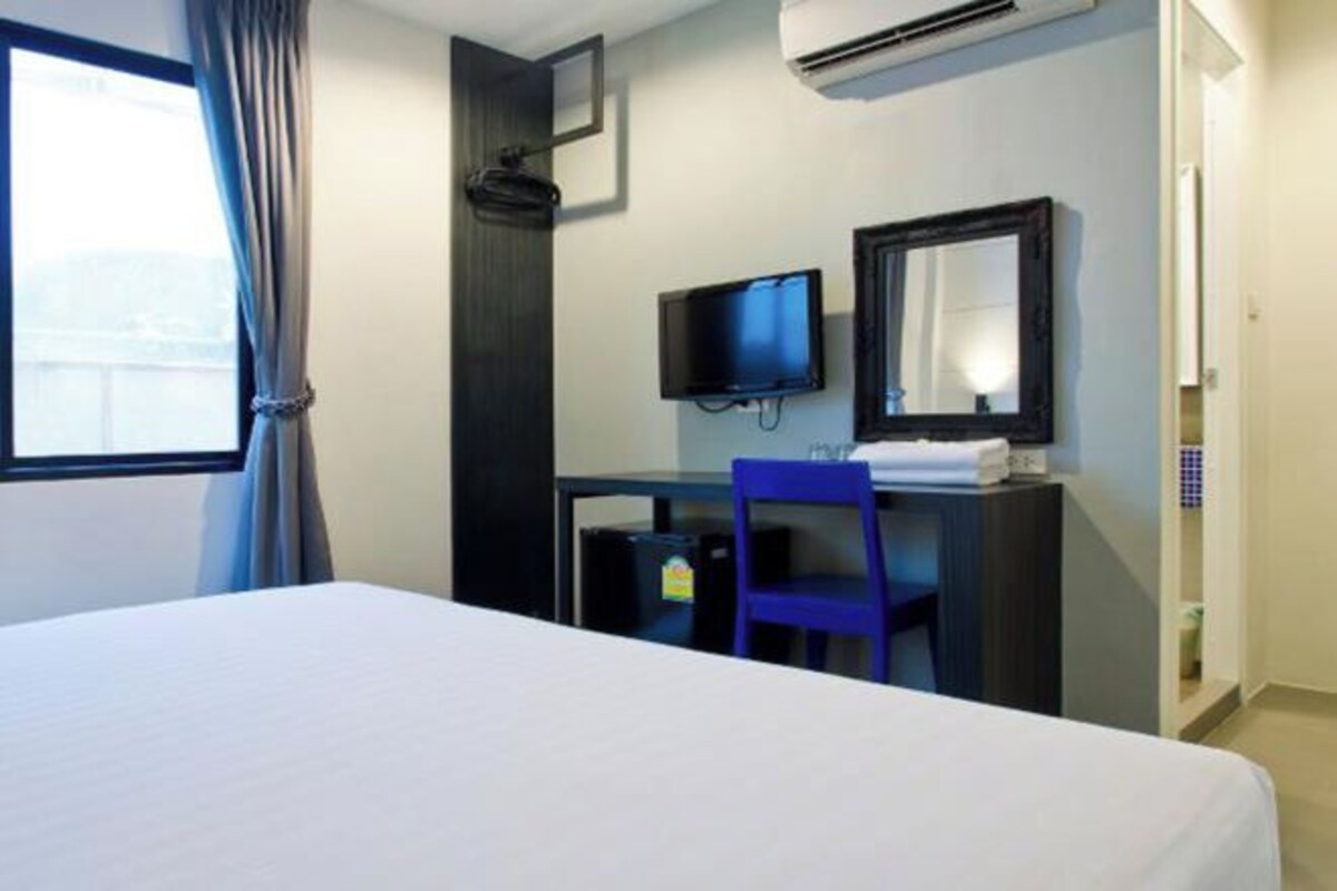 A hotel room with a bed, a desk with a chair, a television, and a mirror.