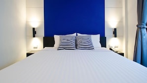 Una habitación de hotel moderna con una cama grande, dos lámparas de noche y una pared azul decorativa.
