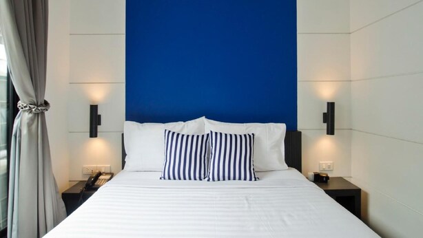 A modern hotel room with a large bed, two bedside tables, a telephone, and a blue accent wall. - DI Place Hotel (Bangkok)