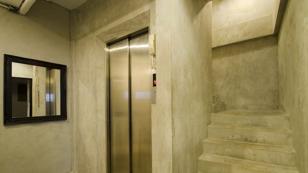 Un pasillo con pared de mármol, un espejo y una escalera que sube a un ascensor.