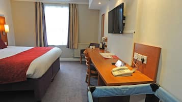 Habitación de hotel con una cama grande, un escritorio de madera con teléfono, una silla y un televisor montado en la pared.
