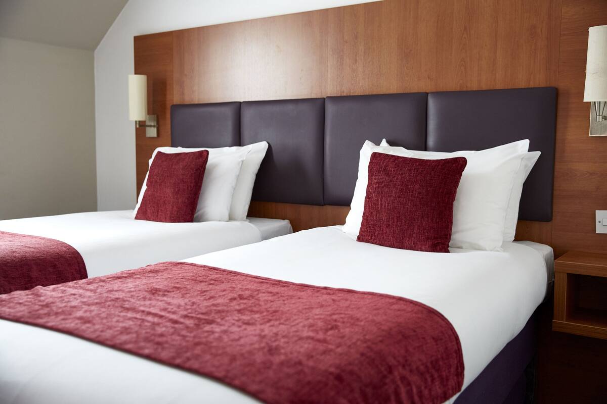 Two beds with red and white bedding, a wooden headboard, and a nightstand with a lamp.