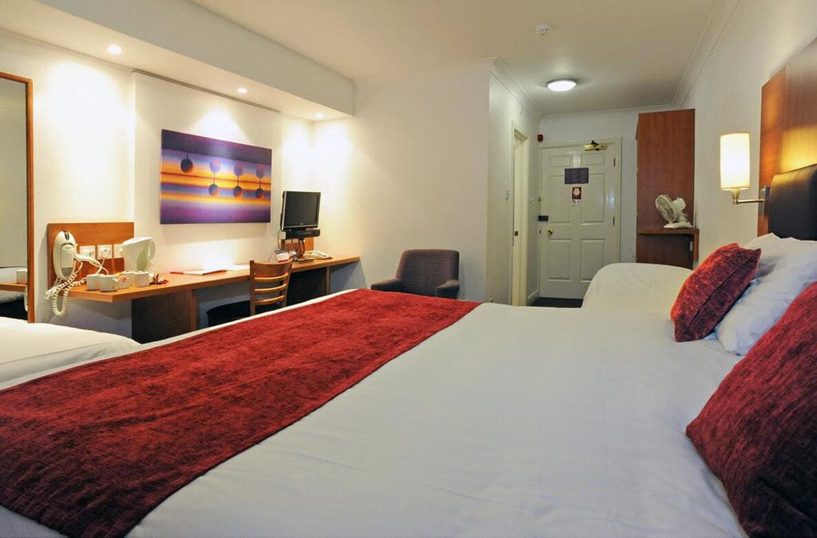 A hotel room with a large bed, a desk with a computer, a chair, and a television.