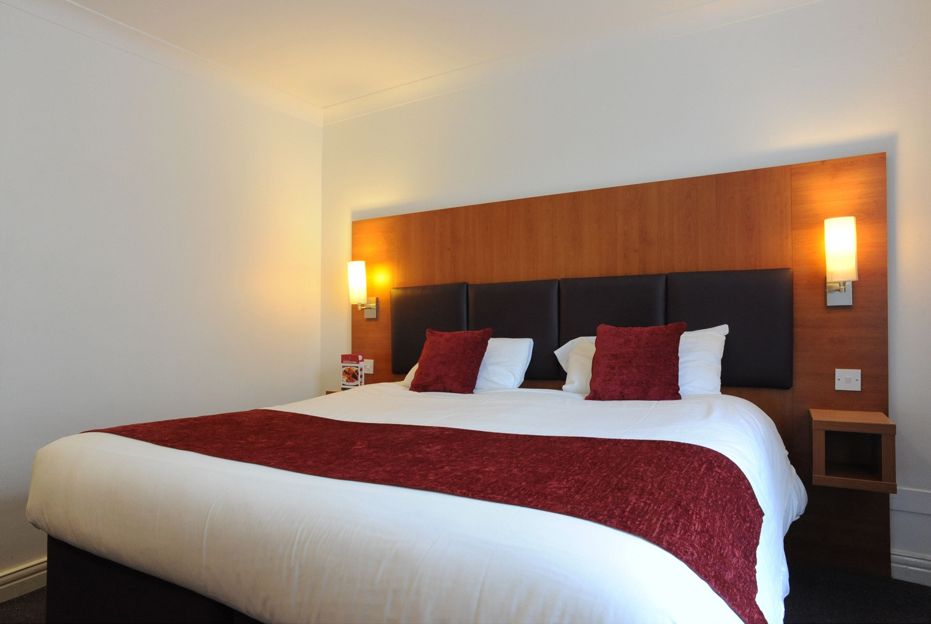 Ein Hotelzimmer mit einem großen Bett, einem Holzkopfende, zwei Nachttischen und Wandlampen.