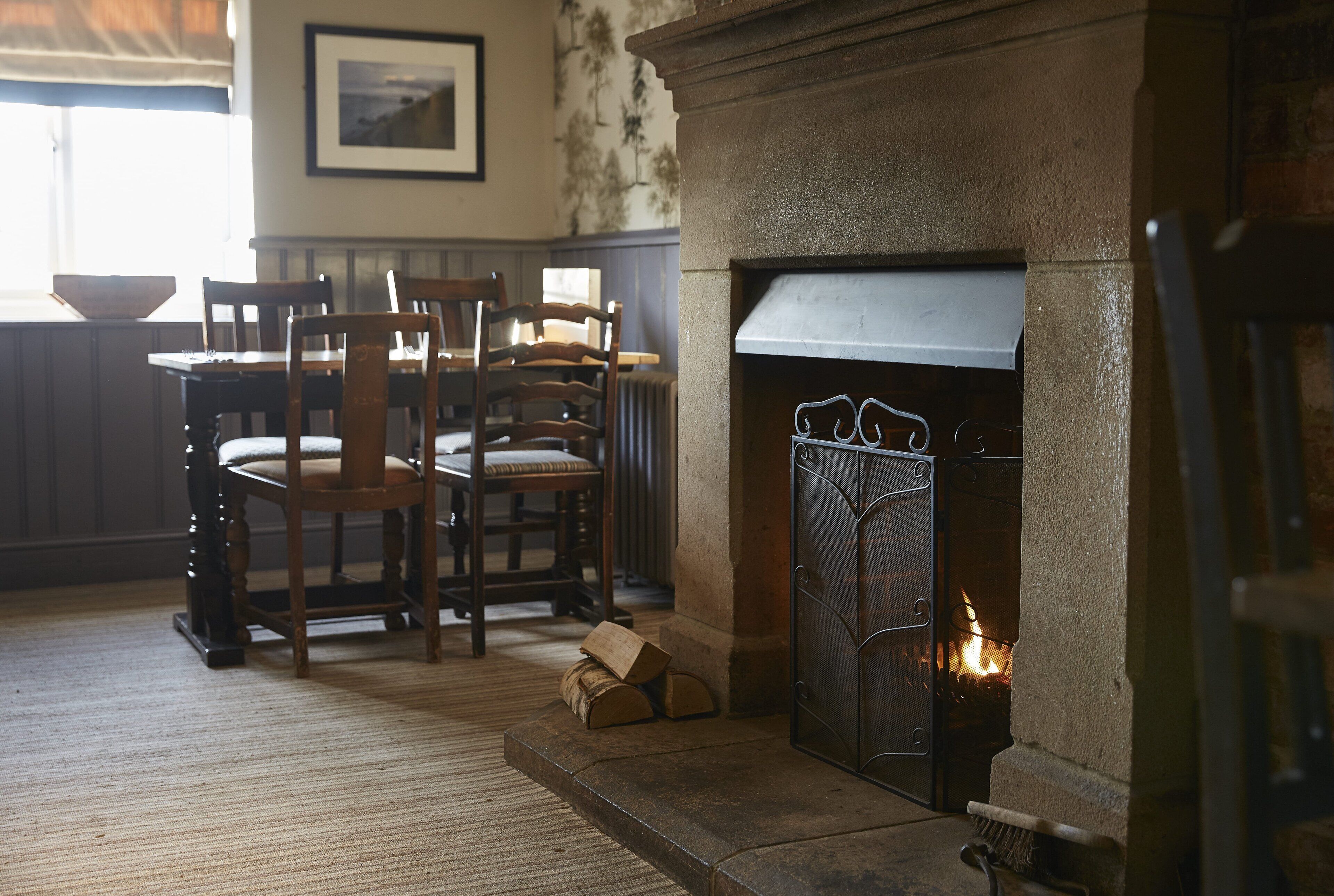 A room with a stone fireplace, wooden chairs, a table, and a framed picture on the wall.