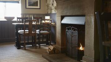 A room with a stone fireplace, wooden chairs, a table, and a framed picture on the wall.