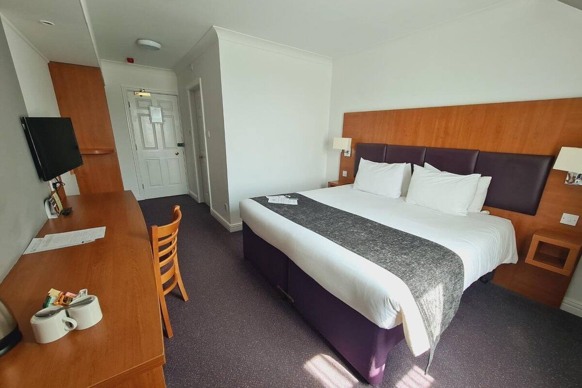 A hotel room with a bed, a desk, a chair, a television, and a door.