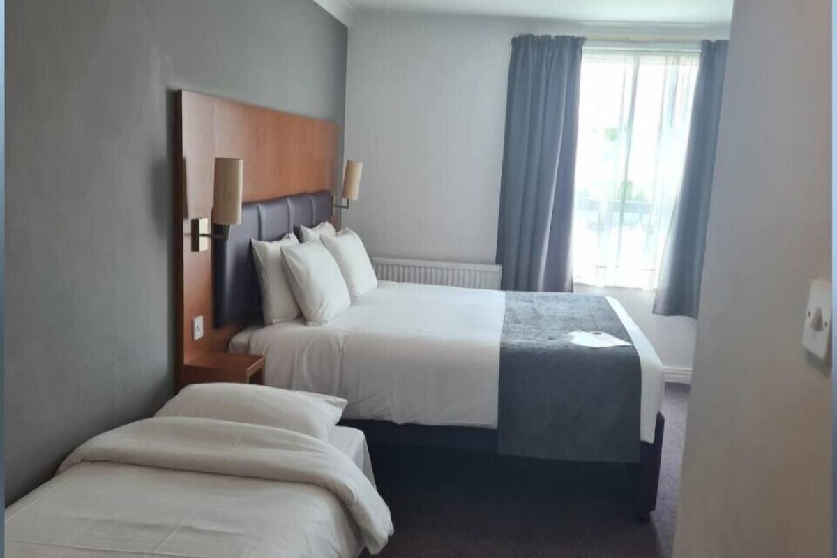 A hotel room with two beds, a wooden headboard, a radiator, and a window with curtains.