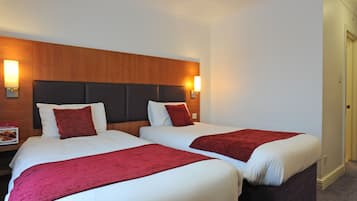 A hotel room with two beds, each with white linens and red throw blankets. There are wall-mounted light fixtures on either side of the headboard.