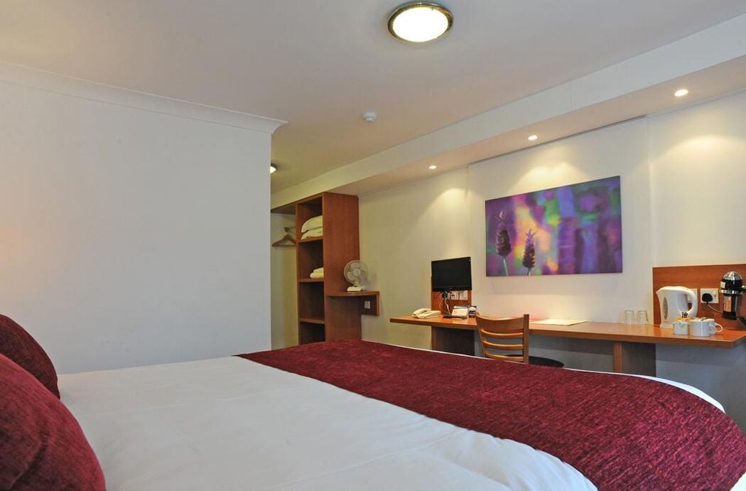 Une chambre d’hôtel avec un grand lit, un bureau avec une chaise, une machine à café et un tableau au mur.