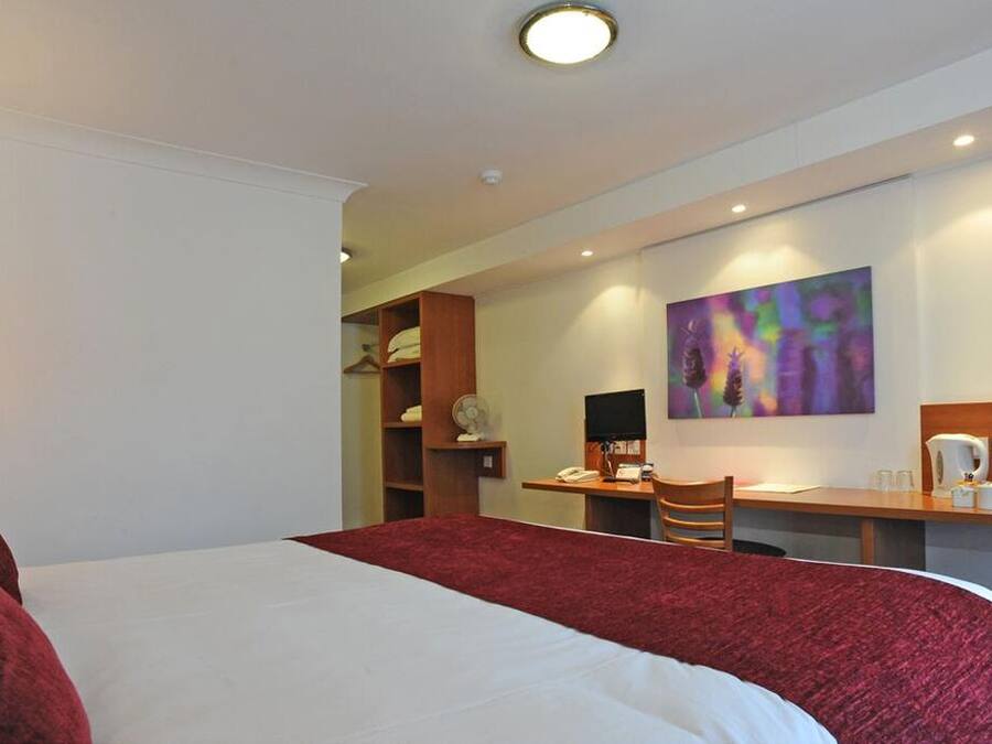Una camera d'albergo con un letto grande, una scrivania con una sedia, una macchina per il caffè e un quadro appeso al muro.