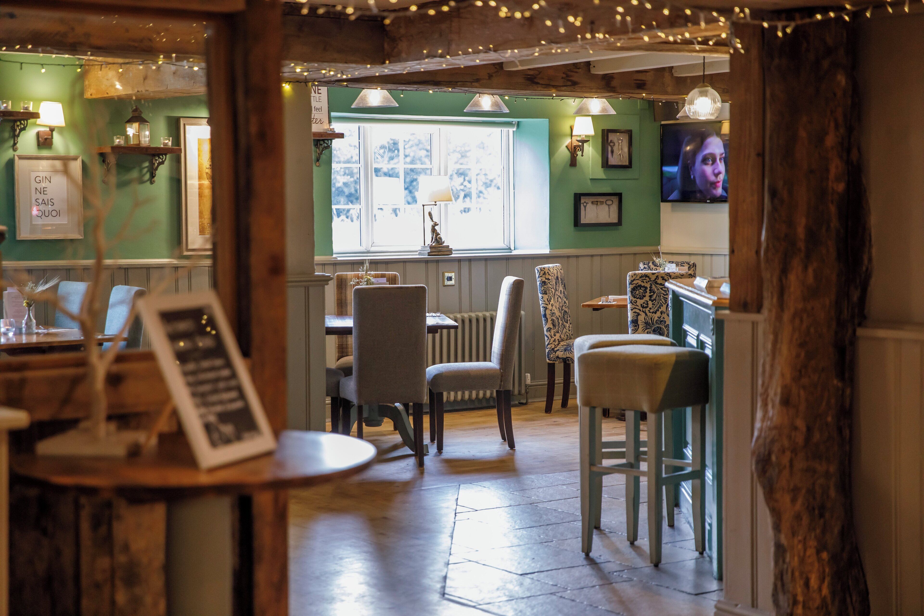Interior acogedor de un restaurante con muebles de madera, iluminación colgante y vistas al exterior a través de una ventana.