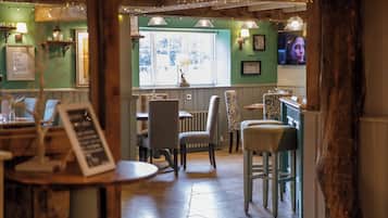 Interior acogedor de un restaurante con muebles de madera, iluminación colgante y vistas al exterior a través de una ventana.