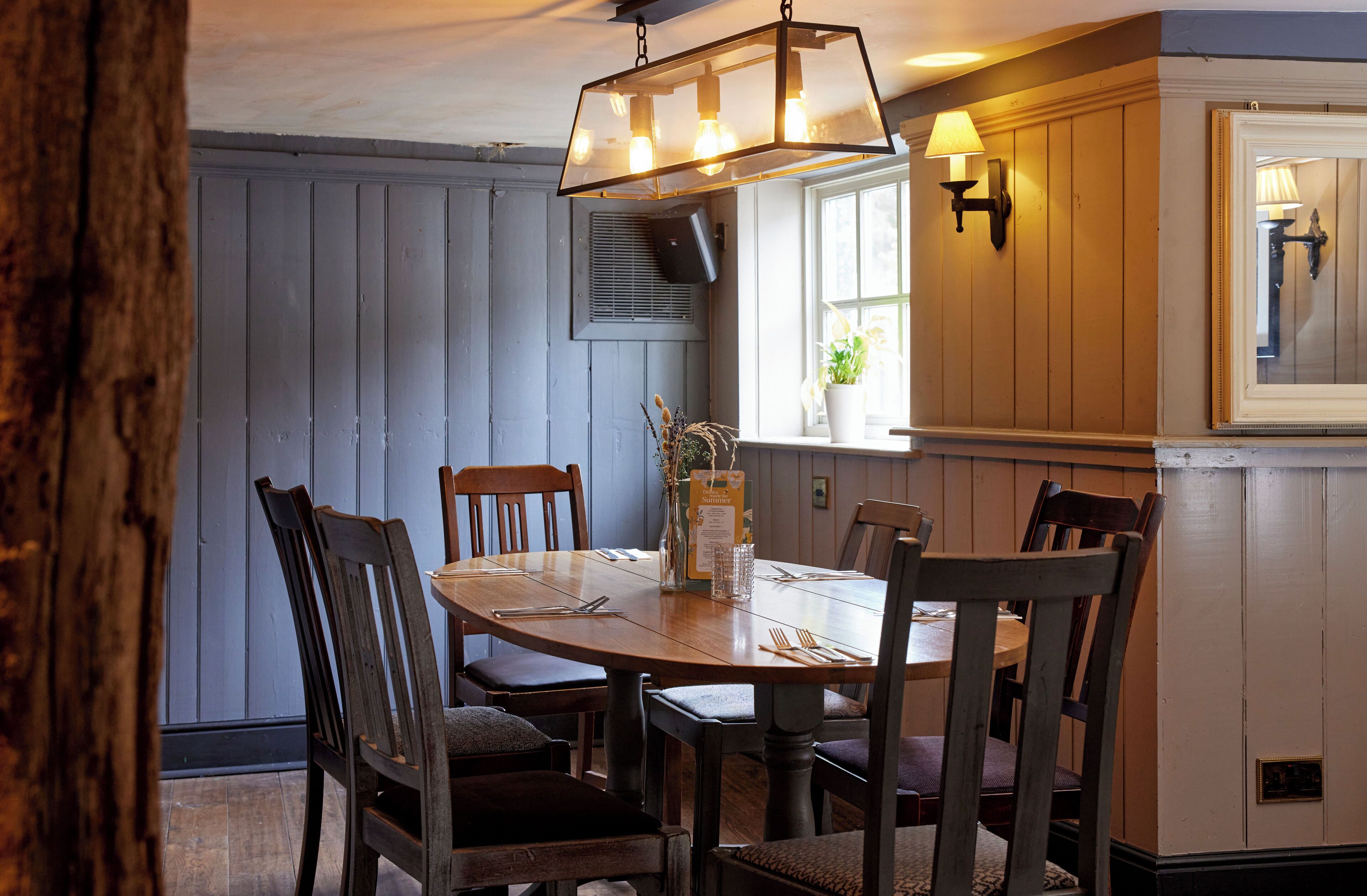 A dining area with a wooden table and chairs, a hanging light fixture, and a window with a view.