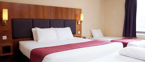 A hotel room with two beds, wooden headboards, and wall-mounted lamps.