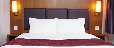 Une chambre d’hôtel avec un grand lit, deux tables de chevet et des lampes fixées au mur.