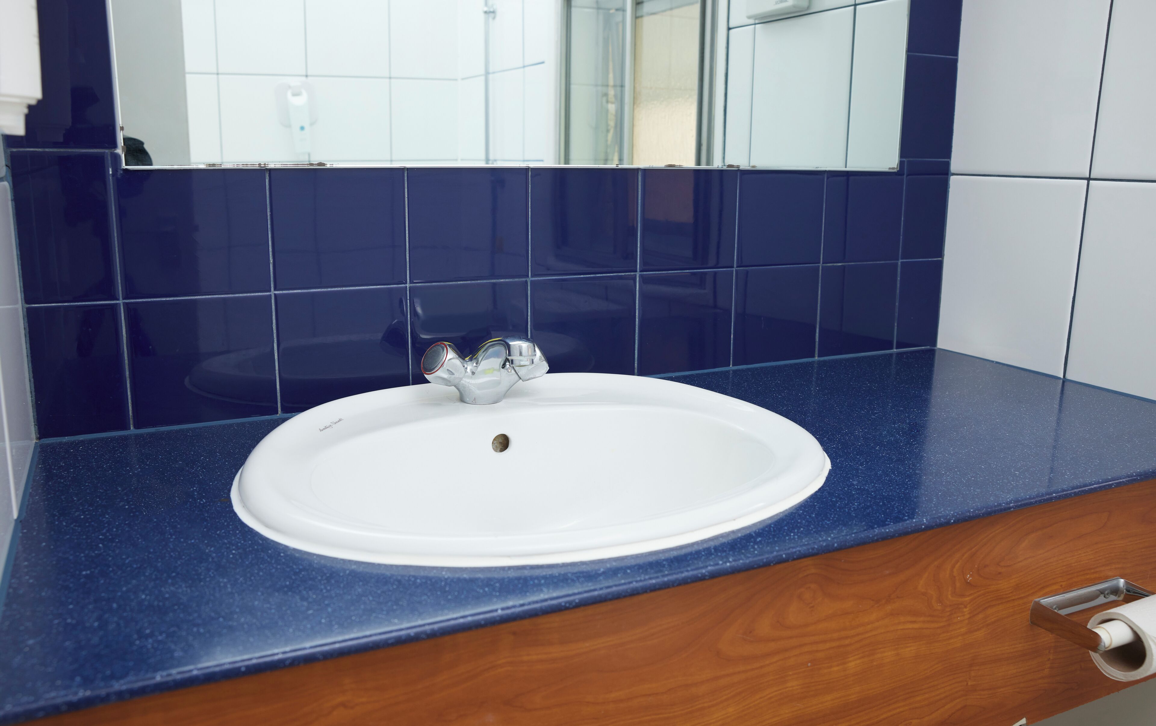 Un baño con un lavamanos blanco, azulejos azules y una encimera de madera.