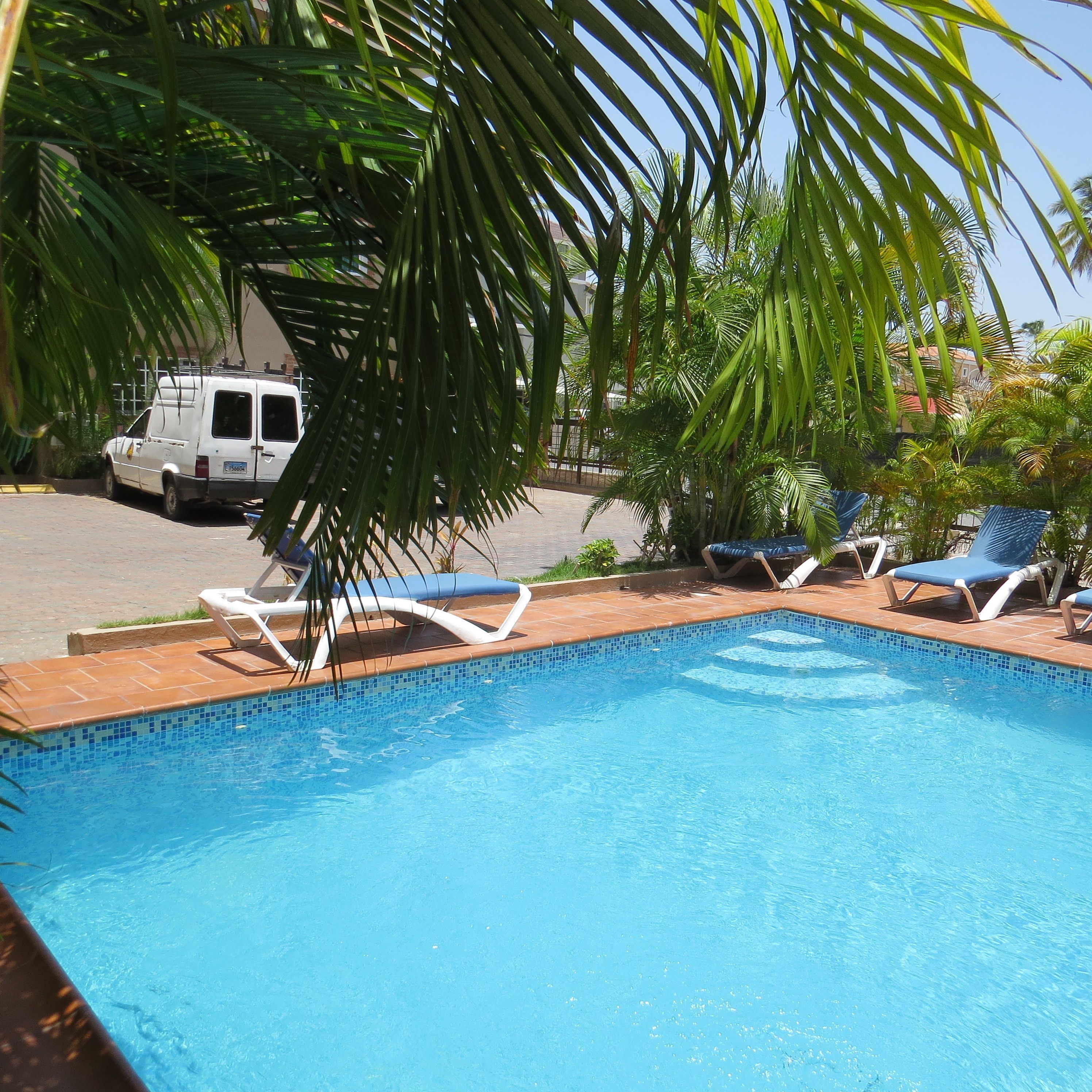Una piscina con sillas de descanso, una camioneta blanca y palmeras.