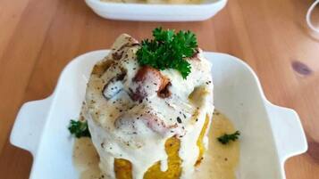Un plato cuadrado blanco con un alimento cubierto de salsa cremosa y adornado con perejil.