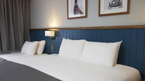 A neatly made bed with white linens and a gray throw blanket. There are two wall-mounted lamps on either side of the bed.