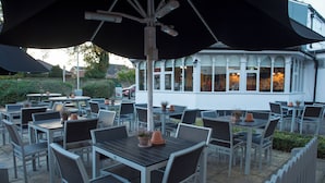 An outdoor patio with tables and chairs, some with potted plants.