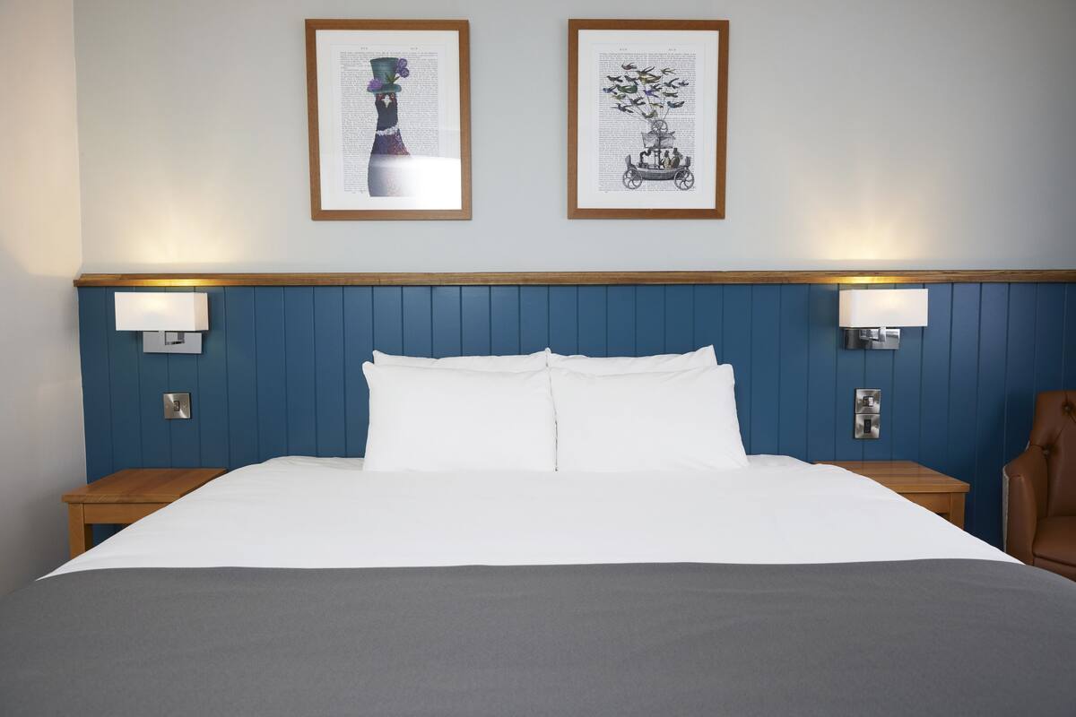 Un lit bien fait, avec du linge de lit blanc, une tête de lit bleue et deux lampes fixées au mur.