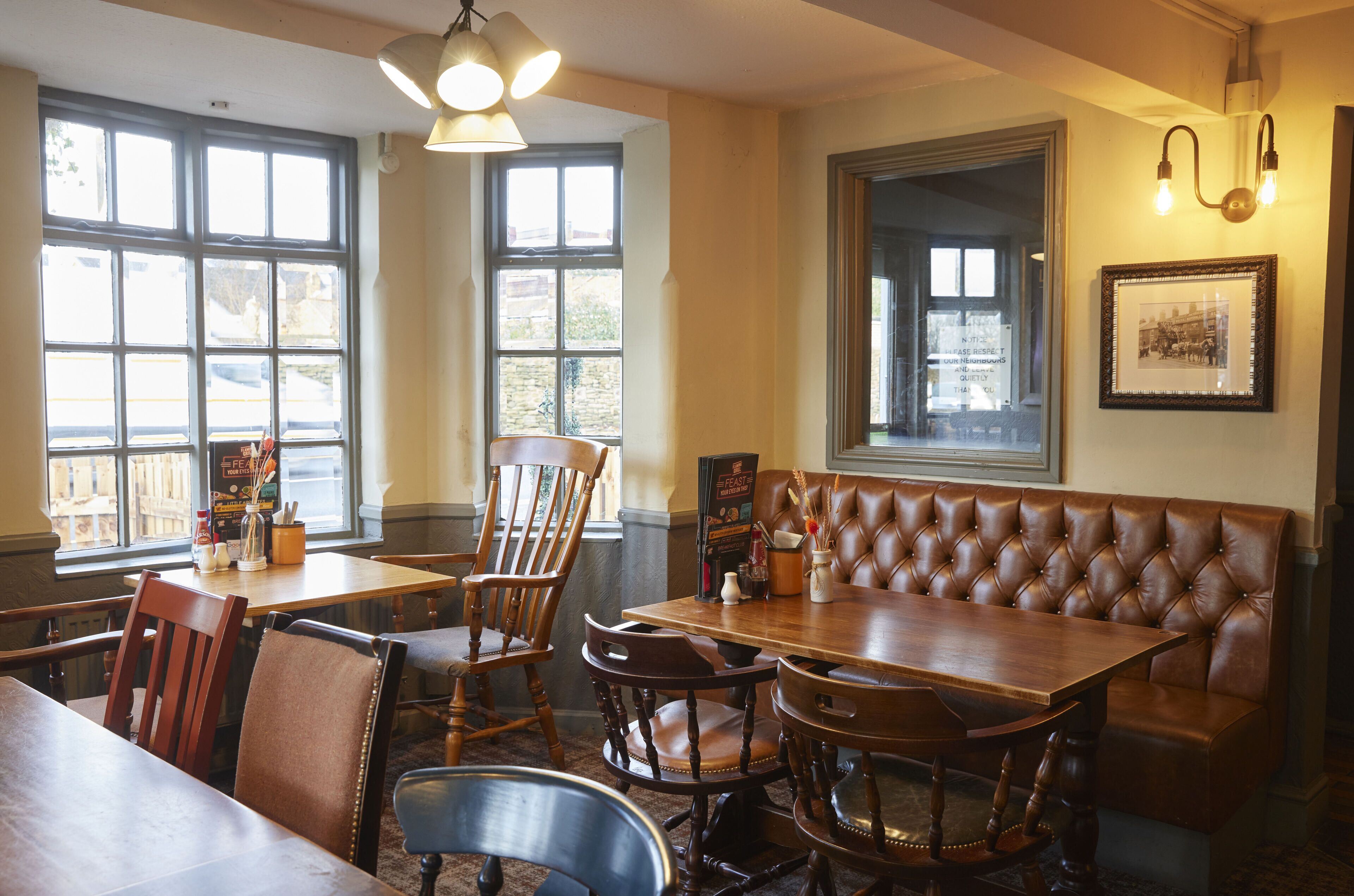 A restaurant interior with wooden tables, leather booths, and large windows.