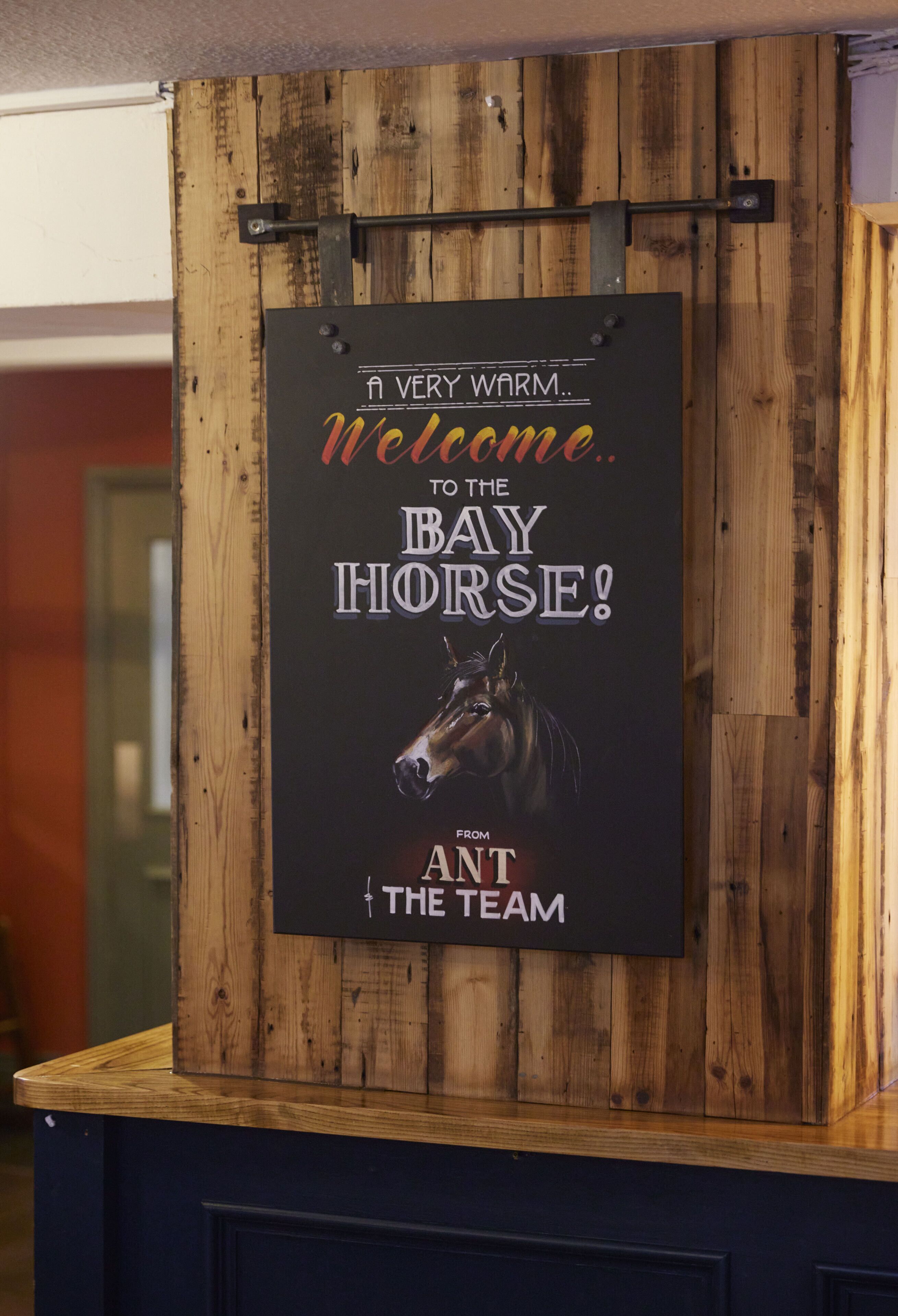 A wooden wall with a sign that reads "A VERY WARM Welcome to the BAY HORSE! FROM THE TEAM".