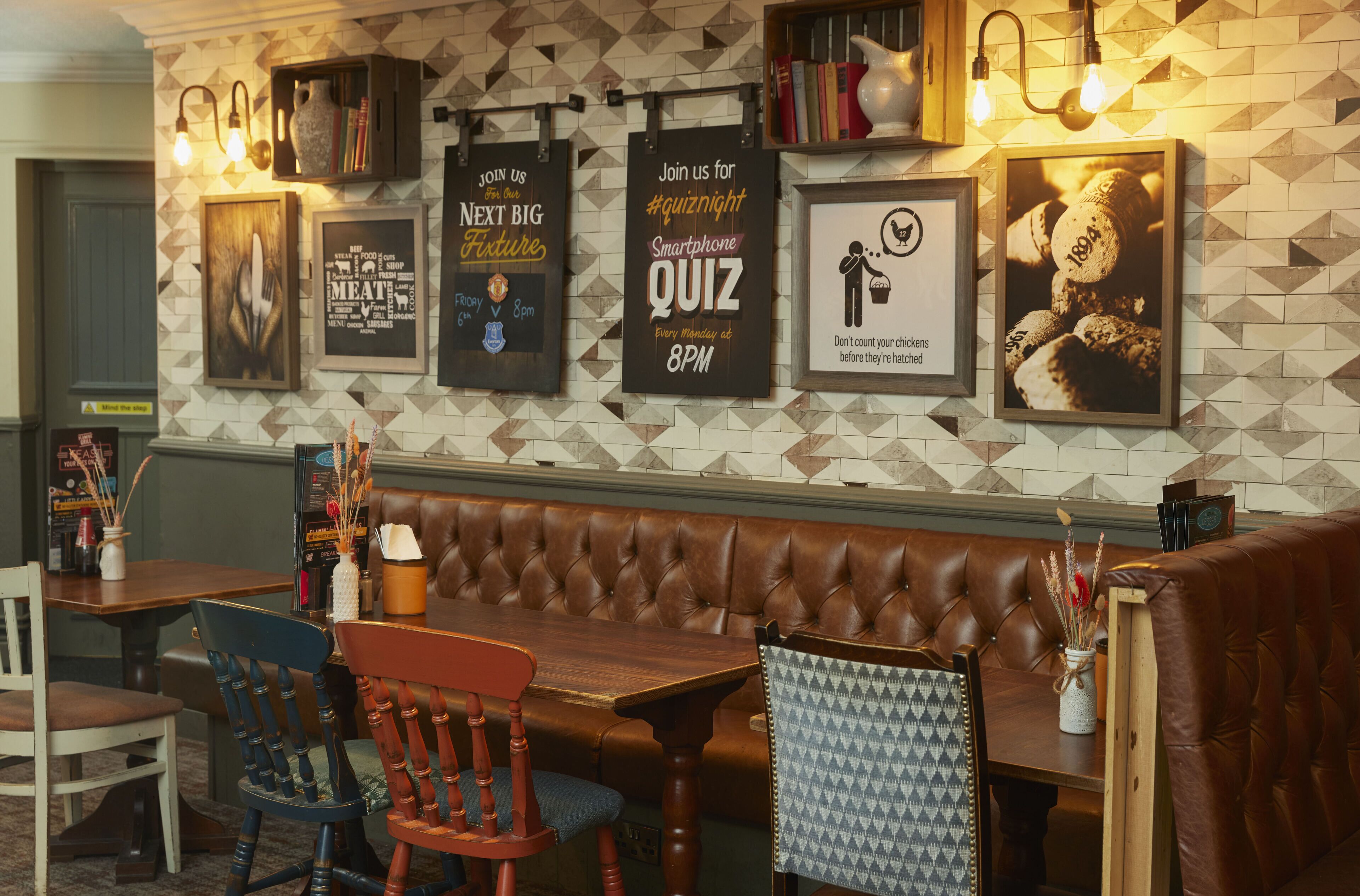 A restaurant interior with a wooden table, leather booth seating, and wall decorations including posters and a framed picture.