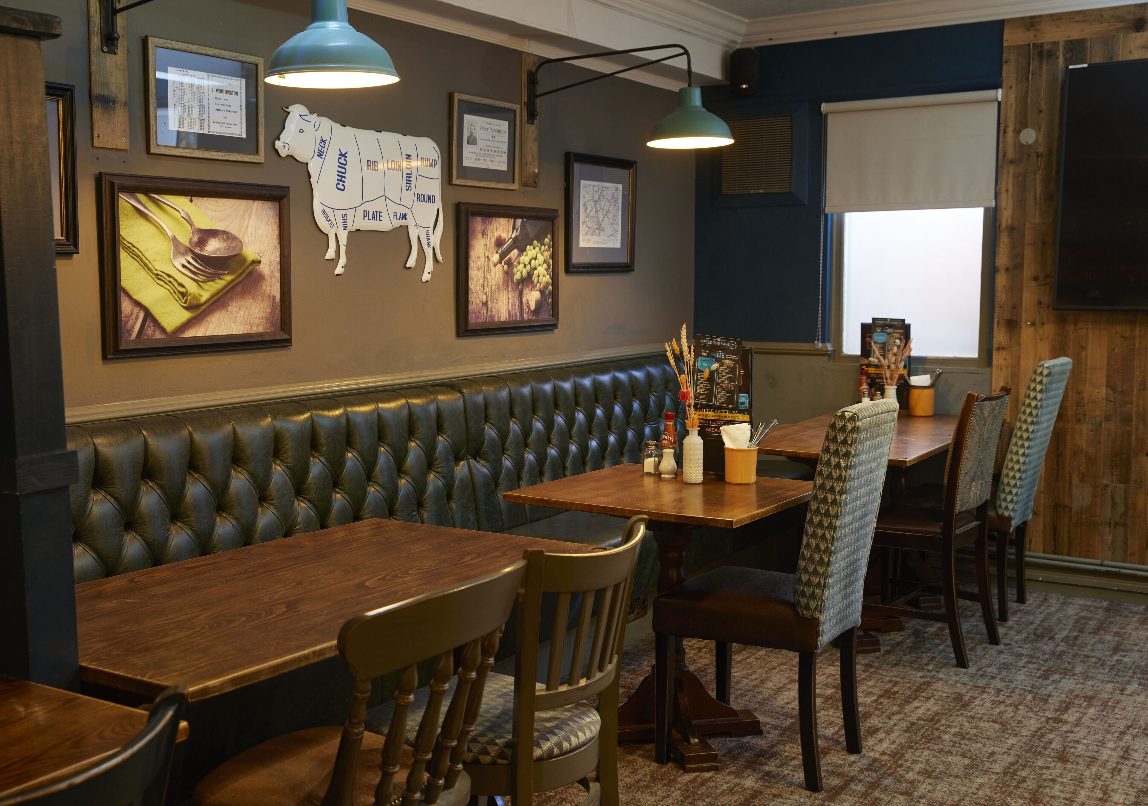 A restaurant with a wooden table, leather booth seating, and framed pictures on the wall.