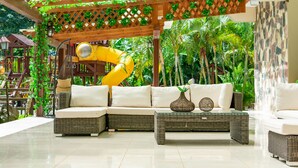 A covered outdoor seating area with wicker furniture, a yellow slide, and lush greenery. - Hotel Gran Jimenoa (Jarabacoa)