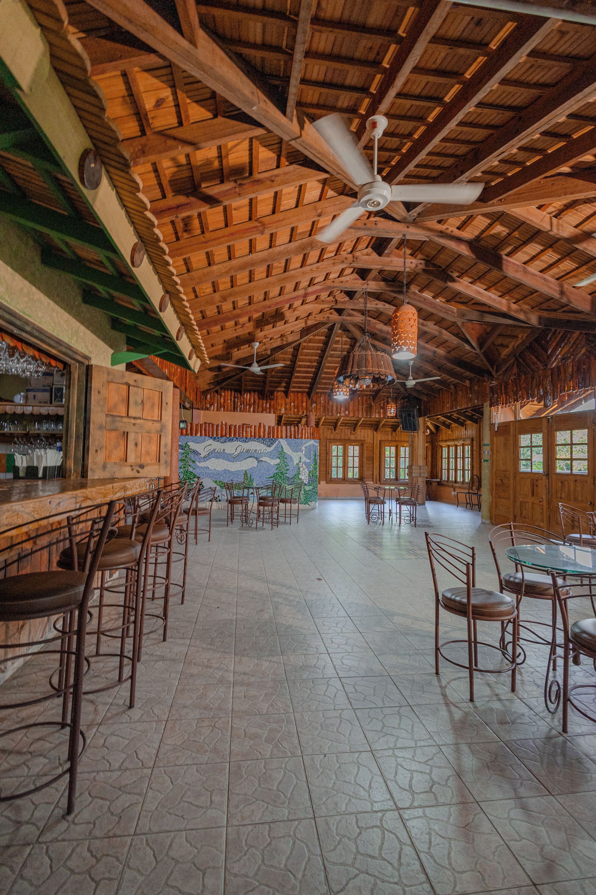 Une pièce spacieuse avec un haut plafond en bois, un coin bar avec des tabourets et une fresque murale.