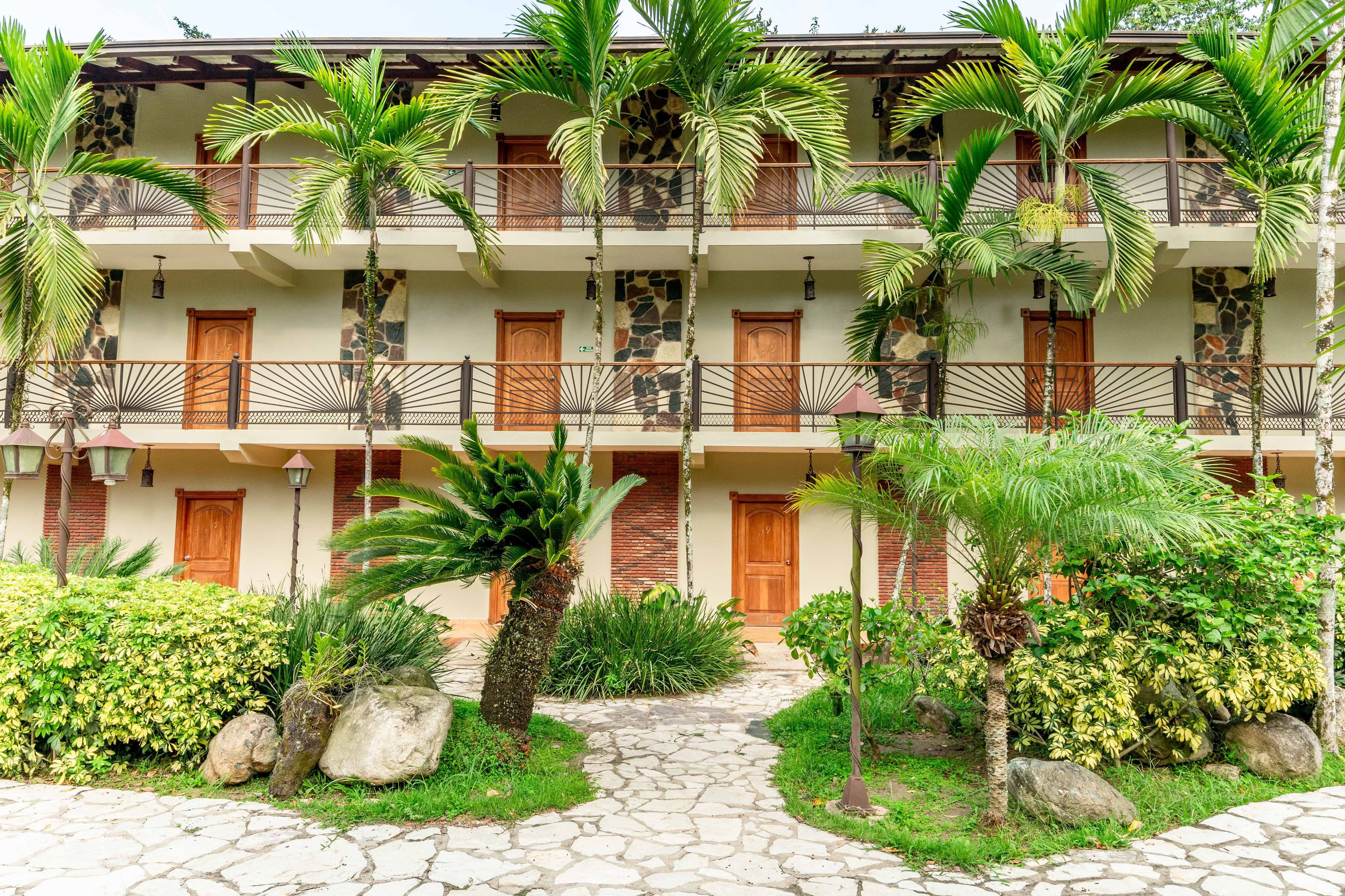 A multi-story hotel with balconies, stone walls, and tropical landscaping.