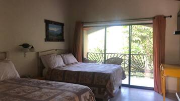 A bedroom with two beds, a window with curtains, a wooden table, and a painting on the wall.