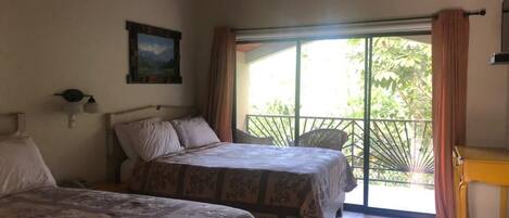 A bedroom with two beds, a window with curtains, a wooden table, and a painting on the wall.