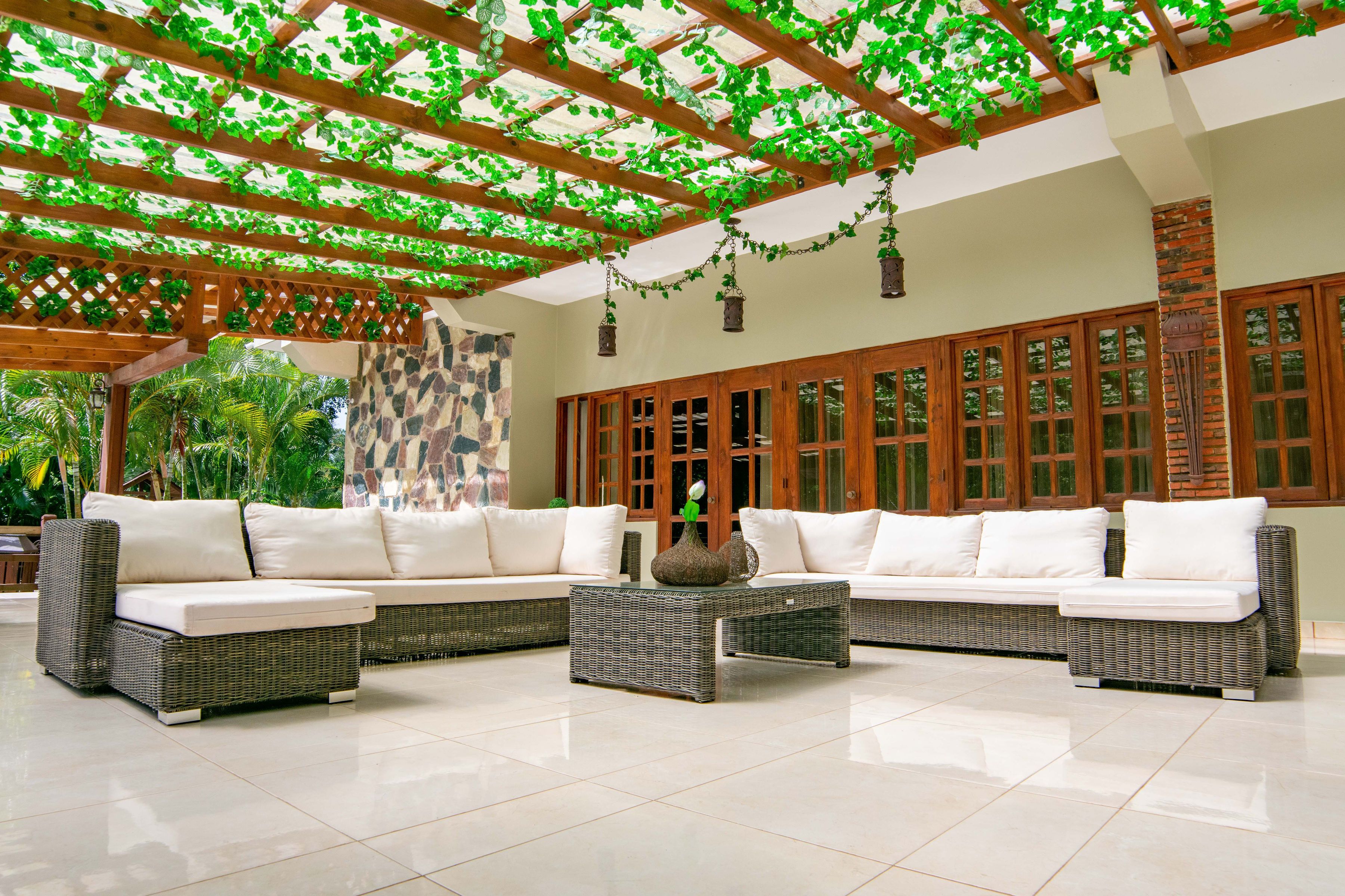 A spacious indoor area with a large sectional sofa, a coffee table, and a pergola with green vines.