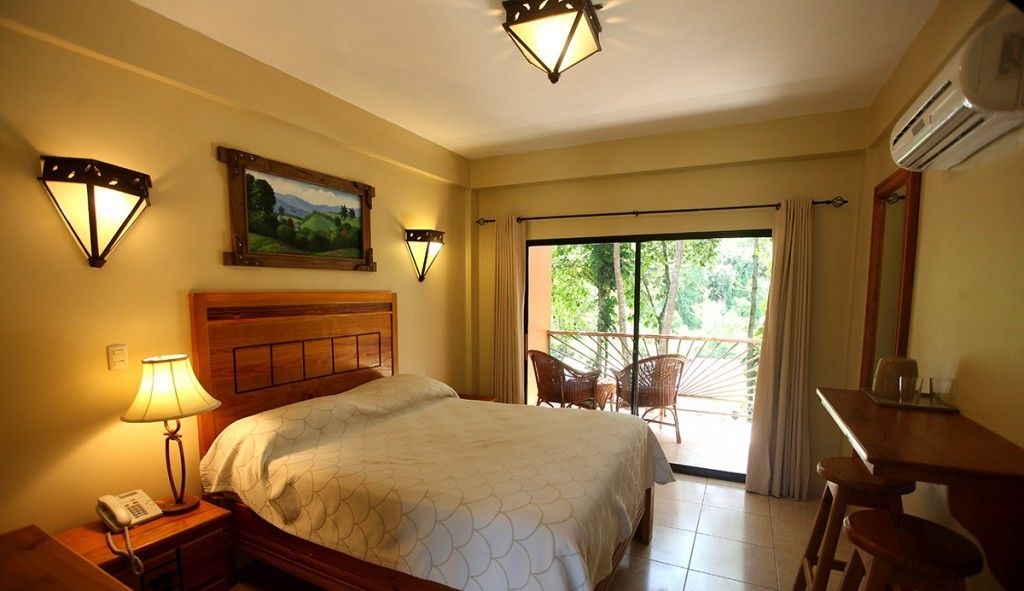 A hotel room with a bed, a desk, a chair, a lamp, and a painting on the wall.