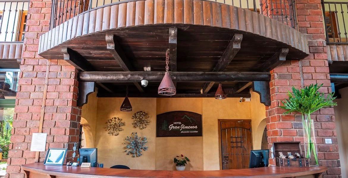 Un espace d’accueil d’hôtel avec un comptoir en bois, une enseigne indiquant « Hôtel Gran Viameño » et une plante en pot.