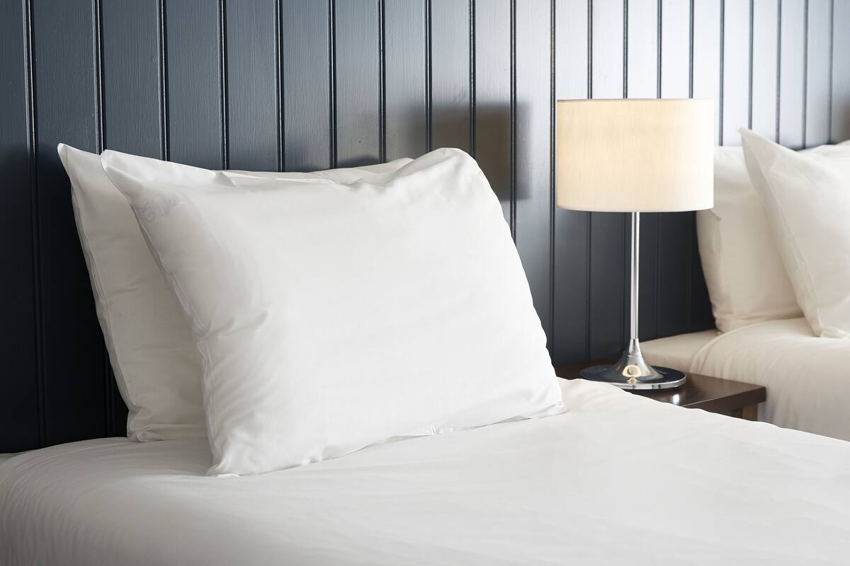A neatly made bed with white bedding and pillows, a bedside table with a lamp, and a dark wooden headboard.