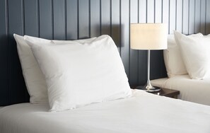 Una cama bien hecha con ropa de cama y almohadas blancas, una mesita de noche con una lámpara y un cabecero de madera oscura.