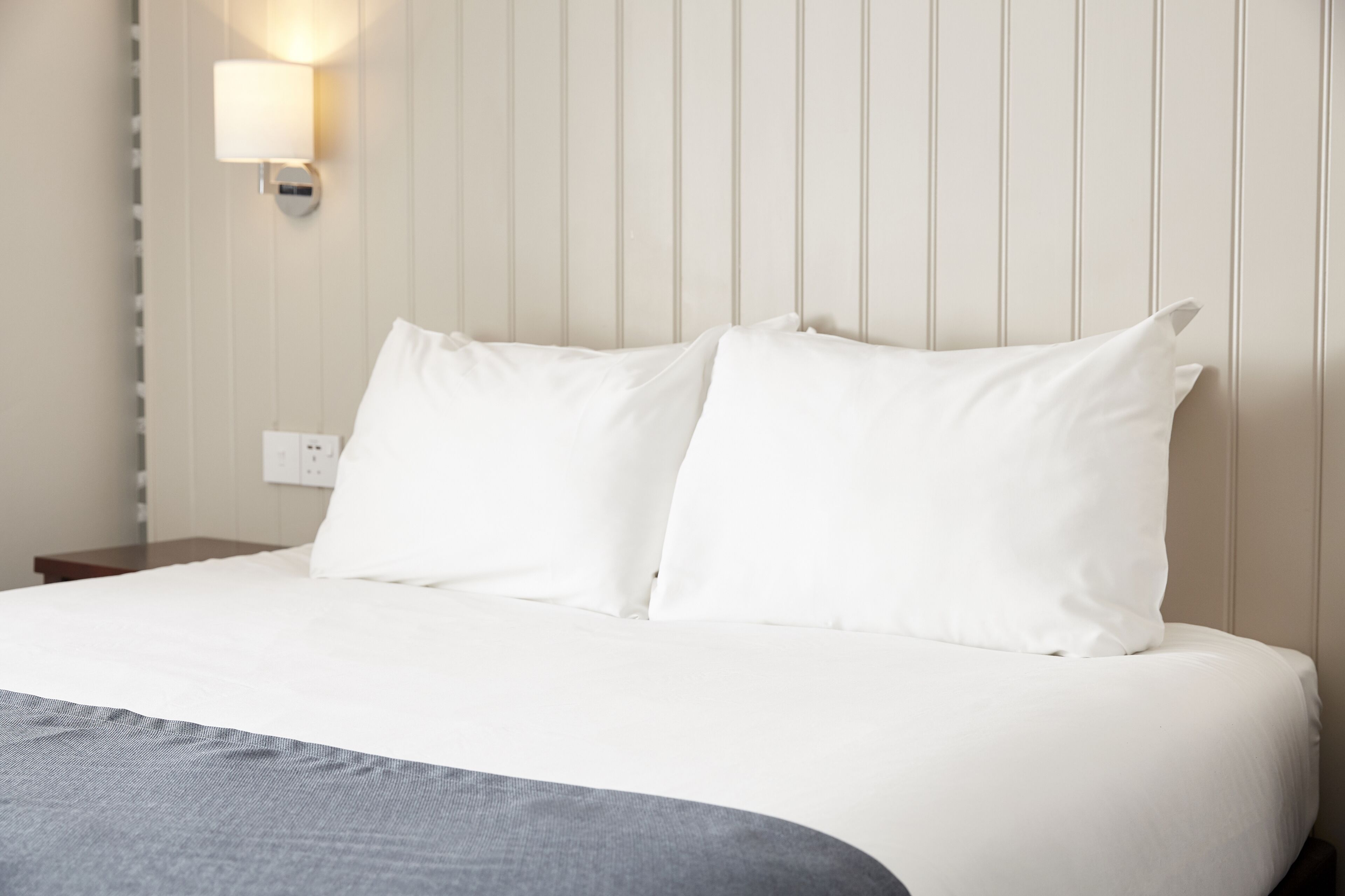 A neatly made bed with white linens and a grey throw blanket.