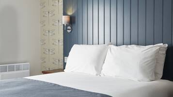 Una cama bien tendida con sábanas blancas en una habitación con cabecera azul y una lámpara de pared.