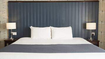 A neatly made bed with white linens and a grey throw blanket, flanked by two bedside tables with lamps, against a wall with a vertical panel design and dragonfly wallpaper.