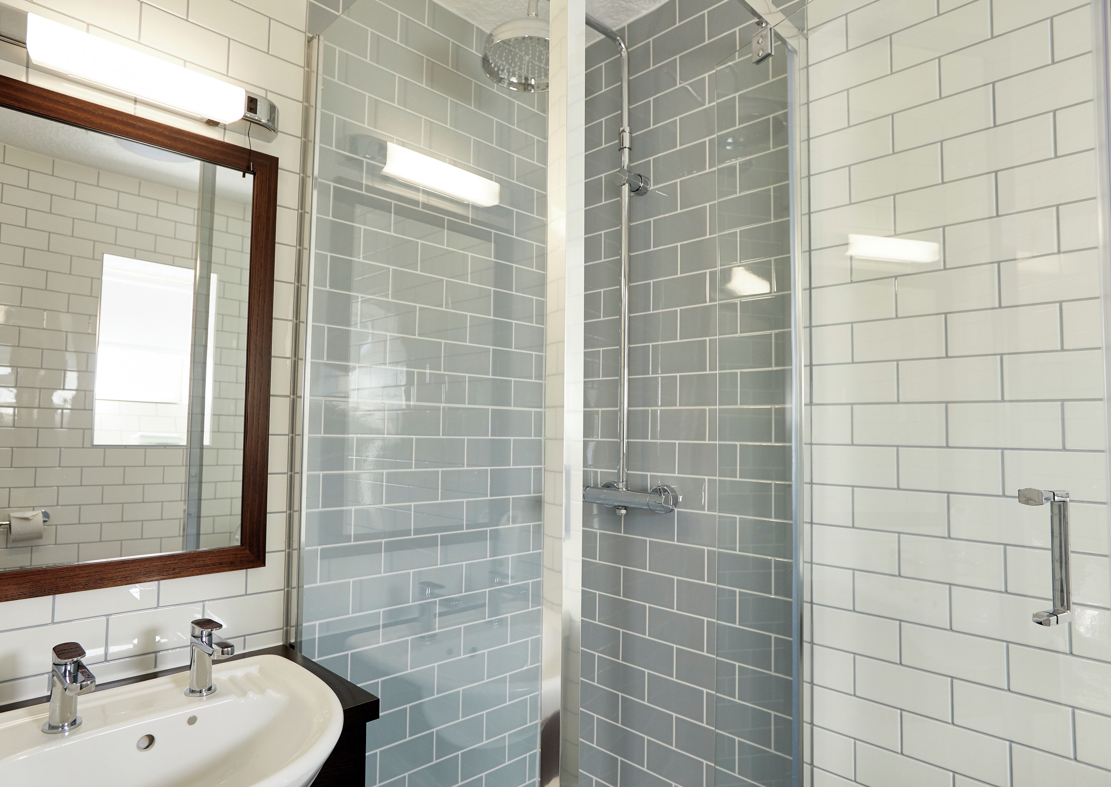 Een moderne badkamer met witte metro tegels, een glazen douchecabine en een spiegel met houten lijst.