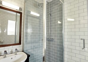 Un baño moderno con baldosas blancas estilo metro, un box de ducha de vidrio y un espejo con marco de madera.