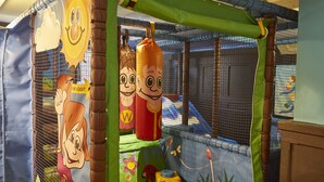 Un área de juegos con decoraciones de personajes de dibujos animados, una jaula de seguridad y estructuras acolchadas.